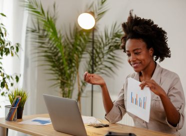 African businesswoman is showing result about market research. Girl with curly hair is working at home, using laptop and showing some results.